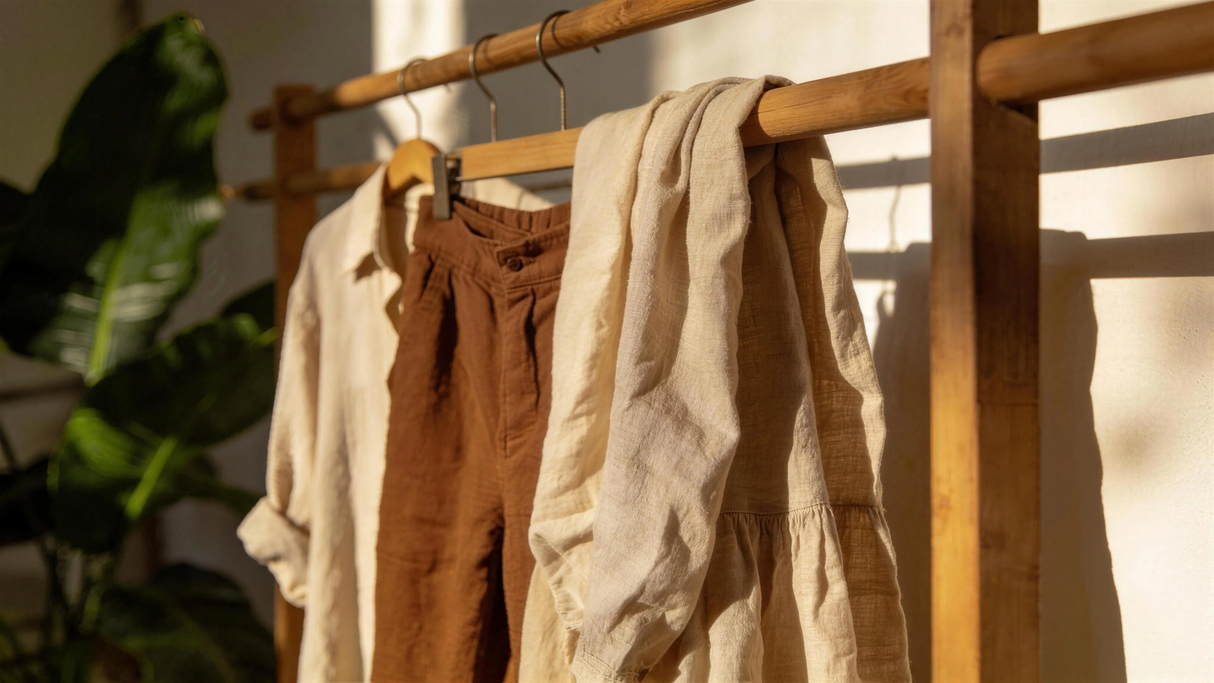 Linen garments hanging from a wooden rack in soft afternoon light.